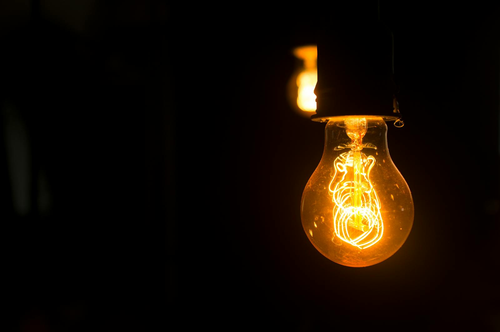 Close-up view of an illuminated vintage light bulb with glowing filament against a dark background.